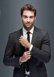Confident man in a dark suit and tie, adjusting his cufflinks against a gray backdrop.